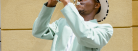 artist dressed in light blue suit and white hat playing the trumpet